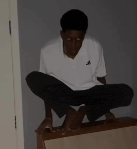 a young man wearing a white adidas shirt squatting on a table