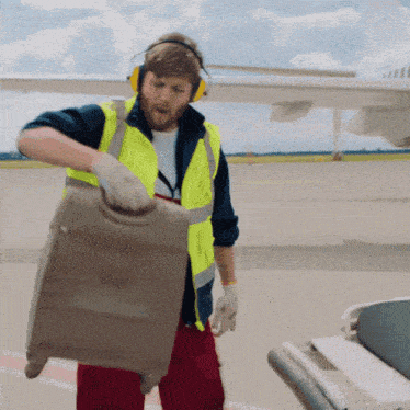 a man wearing headphones and a yellow vest is pulling a suitcase