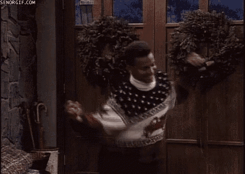a man in a sweater is standing in front of a door with christmas wreaths .