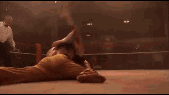 a man is laying on the ground in a wrestling ring while another man is standing behind him .
