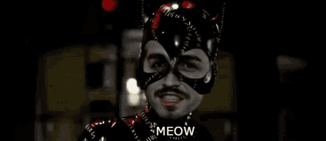 a man in a catwoman costume is standing in the dark and says meow .