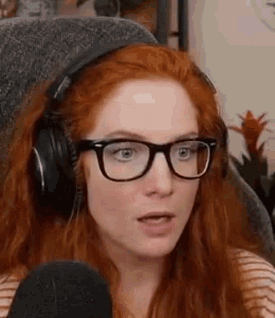 a woman with red hair is wearing headphones and glasses while sitting in front of a microphone .