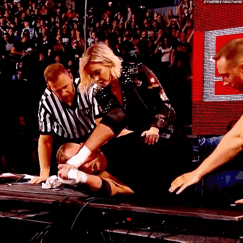 a man is laying on a table with a referee and a woman standing next to him .