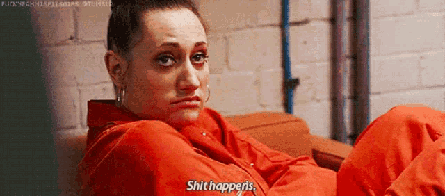 a woman in an orange jumpsuit is laying on a couch and says `` shit happens '' .