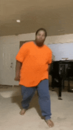 a man in an orange shirt is dancing in a room
