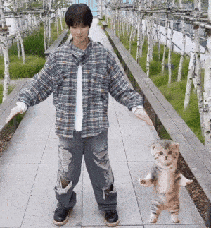 a man in a plaid shirt and ripped jeans is holding a small cat