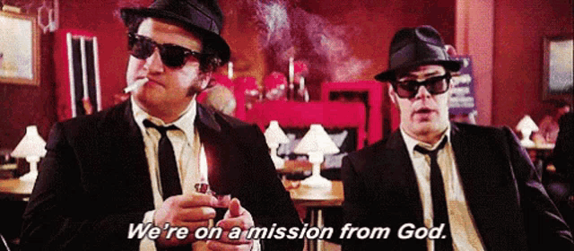two men in suits and hats are smoking cigarettes and saying we 're on a mission from god .