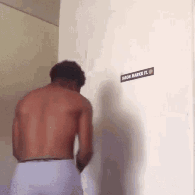 a shirtless man is standing in front of a wall with a sticker on it that says jason mark it .