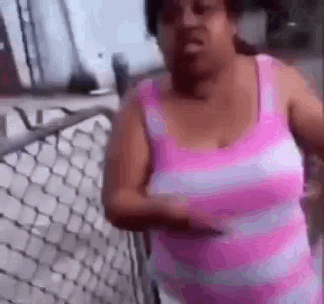 a woman is standing in front of a chain link fence wearing a pink tank top .