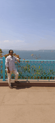 a man standing in front of a blue fence overlooking the ocean