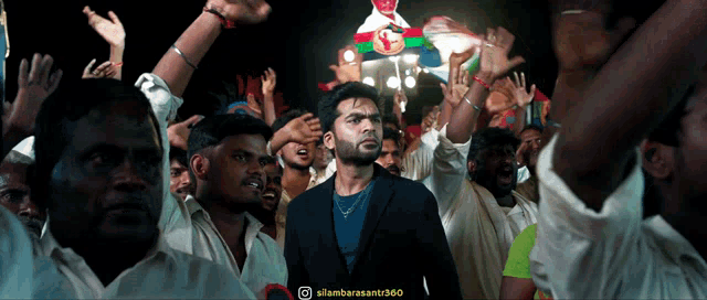 a man in a suit stands in front of a crowd of people with their hands in the air ..