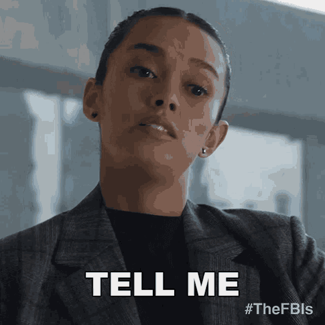 a woman in a suit says " tell me "