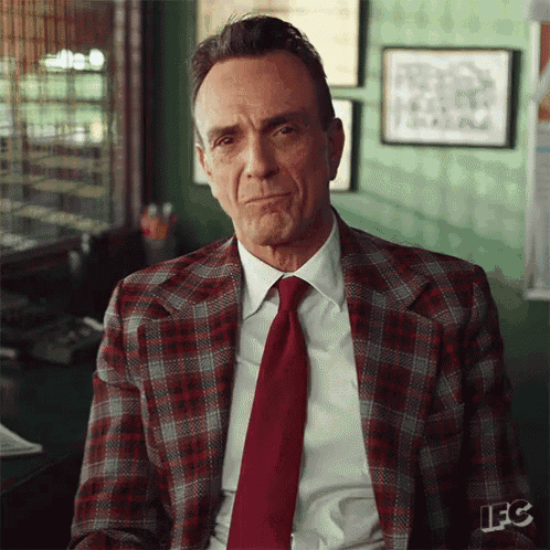 a man in a plaid suit and red tie is sitting at a desk in an office .