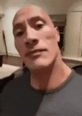 a bald man is making a funny face while wearing a blue shirt and looking at the camera .