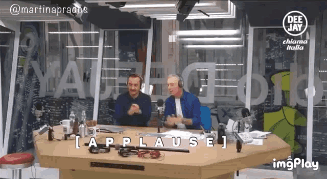 two men are sitting at a table in front of a deejay sign