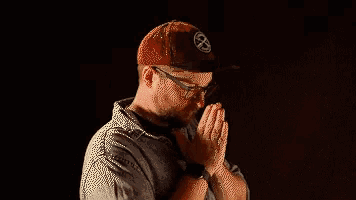 a man wearing a hat and glasses is praying with his hands folded in front of him .