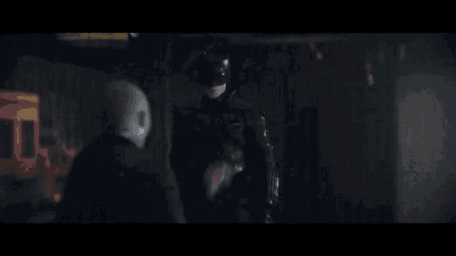 a man in a batman costume is fighting another man in a dark room with a sword .