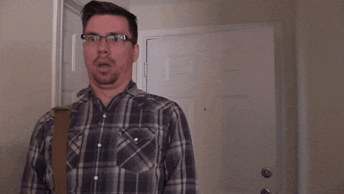 a man wearing glasses and a plaid shirt is standing in front of a door