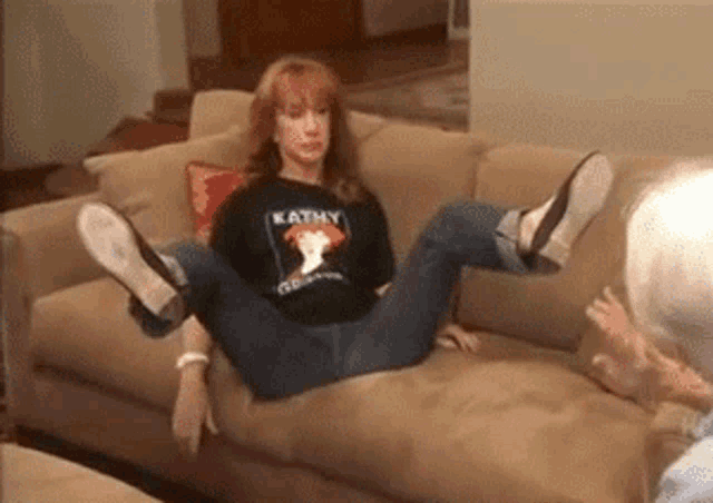 a woman is sitting on a couch wearing a kathy t-shirt