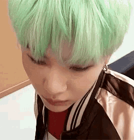 a close up of a person 's face with green hair and a jacket .