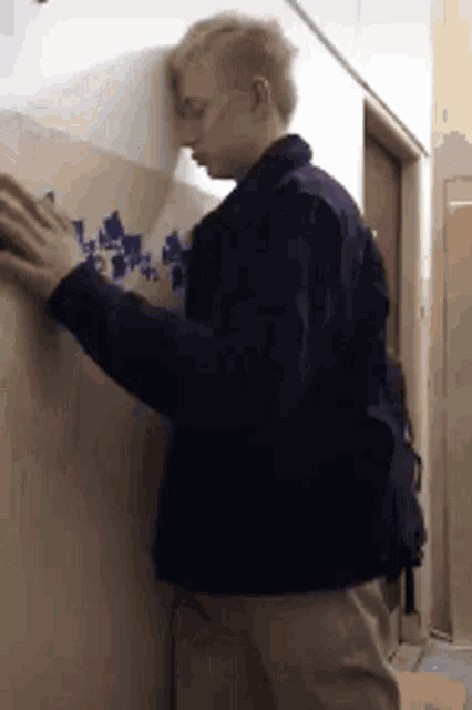 a young man is leaning against a wall with his hands .