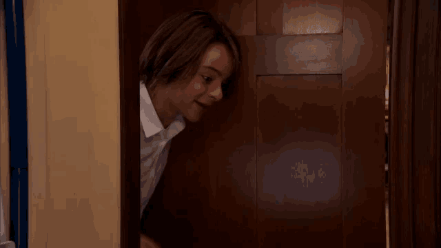 a woman is peeking out from behind a wooden door and giving a thumbs up .