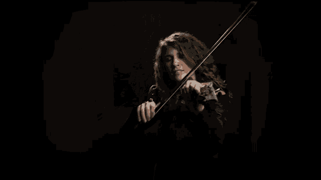 a woman is playing a violin in the dark