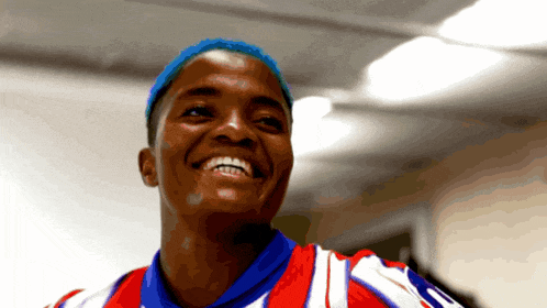 a woman with blue hair is smiling and wearing a red white and blue shirt