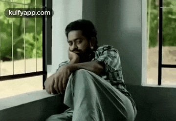 a man is sitting on a window sill looking out .