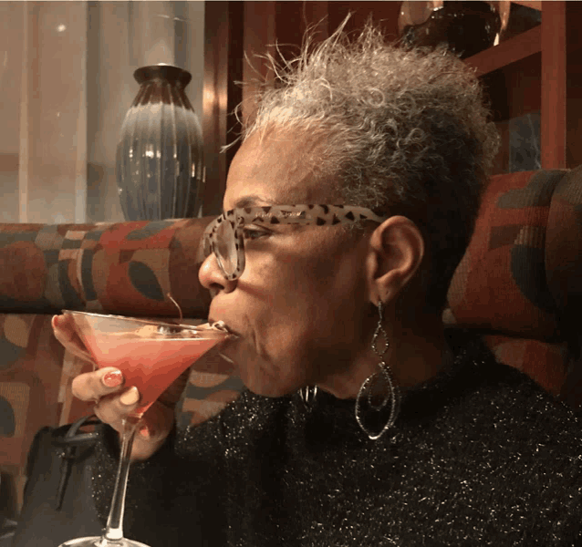 a woman wearing glasses and earrings drinks a martini