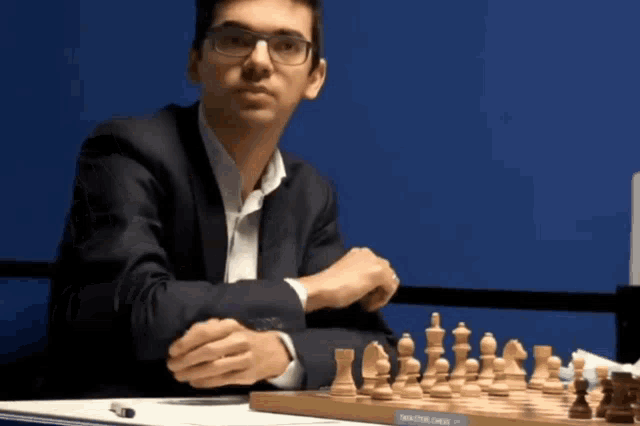 a man in a suit sits in front of a chess board that says " solving chess "