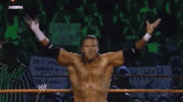 a shirtless wrestler is standing in a wrestling ring with his hands on his hips .