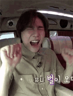 a man is sitting in a car with his mouth open and his hands up .