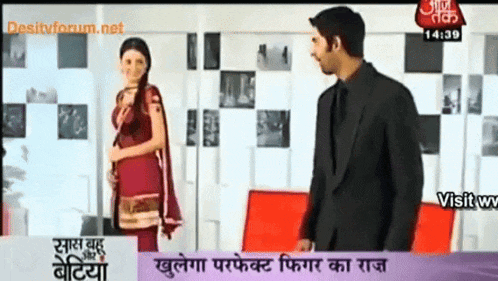 a man in a suit stands next to a woman in a red dress on a tv screen