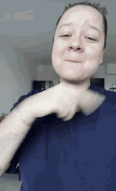 a woman is wearing a blue shirt and making a funny face with her hands .