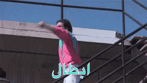 a man in a pink shirt is standing on a set of stairs with arabic writing behind him