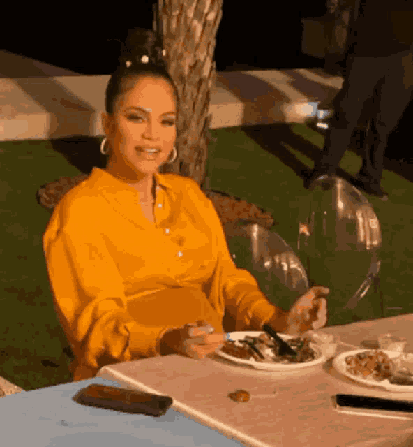 a woman in a yellow shirt sits at a table with plates of food