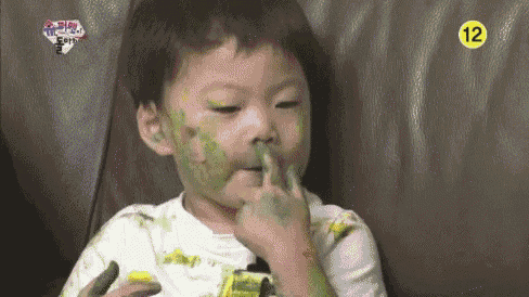 a little boy with green paint on his face is sitting on a couch eating a cucumber .