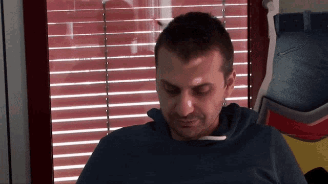 a man is sitting in front of a window with red blinds