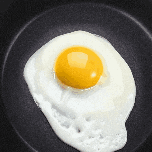 a close up of a fried egg in a black pan