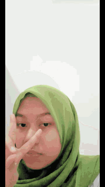 a woman wearing a green hijab making a peace sign