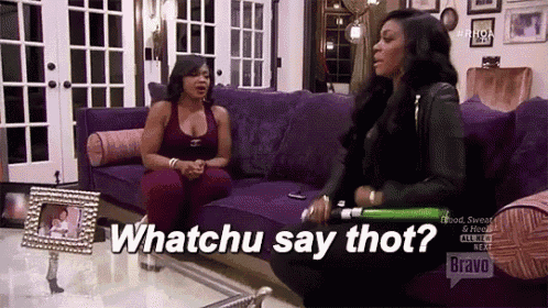 two women are sitting on a couch and one of them is holding a bat and the other is asking whatchu say thot .
