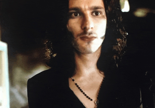 a man with long hair is wearing a necklace