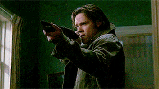 a man in a jacket is pointing a gun at a window .