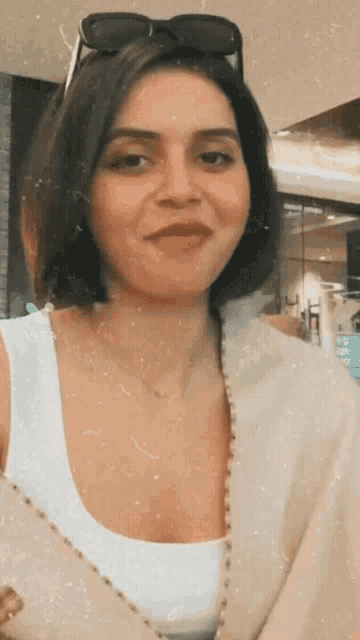 a woman wearing sunglasses and a white tank top smiles