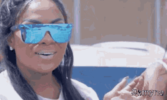 a woman wearing sunglasses and a white shirt is smiling and looking at the camera .