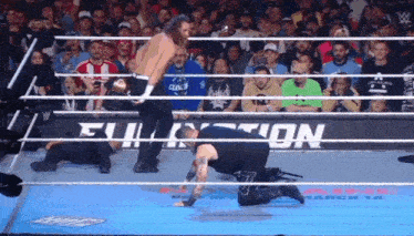 a man is kneeling down in a wrestling ring while a crowd watches .