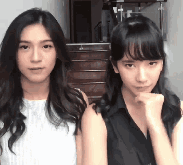 two young women are standing next to each other and one has her fist on her chin