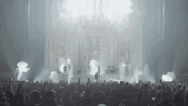 a crowd of people are standing in front of a stage at a concert with smoke coming out of it .