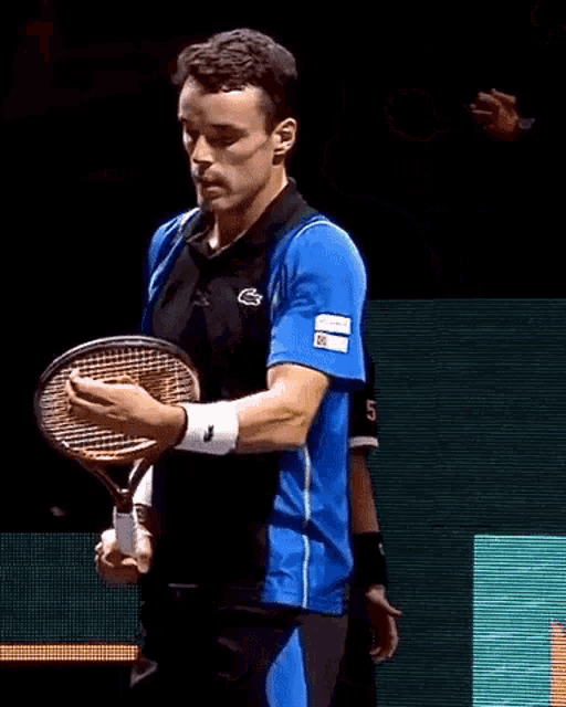 a man holding a tennis racquet with the letter g on his shirt